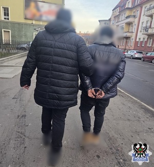 policjant nieumundurowany prowadzi zatrzymanego, który ma złażone kajdanki na ręce trzymane z tyłu