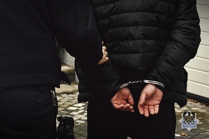 Na zdjęciu policjant prowadzi przykładowego zatrzymanego mężczyznę.