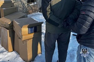 Na zdjęciu zabezpieczone kartony z nielegalnymi papierosami oraz policjant i zatrzymany mężczyzna.