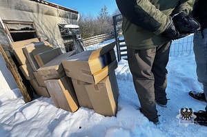 Na zdjęciu zabezpieczone kartony z nielegalnymi papierosami oraz policjant i zatrzymany mężczyzna.