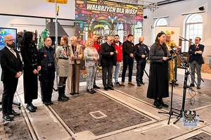 Na zdjęciu policjant w grupie osób podczas konferencji prasowej.