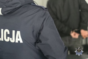 Na zdjęciu policjant oraz kajdanki na rękach przykładowego zatrzymanego.