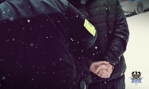 Na zdjęciu policjant prowadzi przykładowego zatrzymanego meżczyznę.