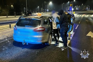 Na zdjęciu policjanci wykonują czynności z zatrzymanymi mężczyznami przy kontrolowanym samochodzie.