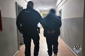 Na zdjeciu policjant prowadzi zatrzymanego mężczyznę.