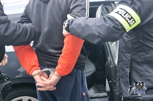 Na zdjęciu policjant zakłada kajdanki zatrzymanemu.