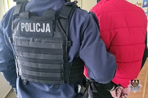 Na zdjeciu policjant pilnuje zatrzymanego mężczyzny.