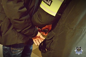 Na zdjęciu policjant zakłada kajdanki zatrzymanemu mężćzyźnie.