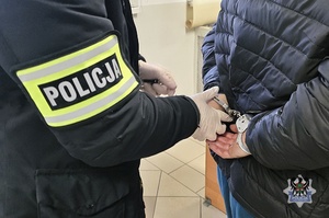 Na zdjęciu policjant zakłada kajdanki zatrzymanemu mężczyźnie.