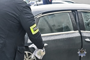 Na zdjęciu policjant umieszcza zatrzymanego mężczyznę w radiowozie .