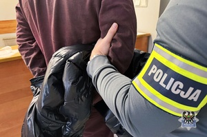 Na zdjęciu policjant pilnuje zatrzymanego mężczyzny.