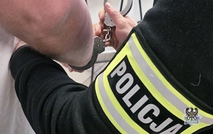 Na zdjęciu policjant zakłada kajdanki przykładowemu zatrzymanemu mężczyźnie.