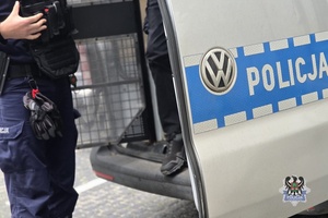 Na zdjęciu policjant zamyka drzwi radiowozu.