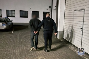 Na zdjęciu policjant prowadzi zatrzymanego poszukiwanego.