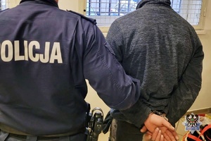 Na zdjęciu policjant pilnuje zatrzymanego mężczyzny.