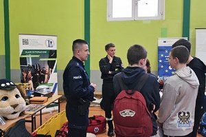 Na zdjęciu policjant w obecności uczestników spotkania promocyjnego.
