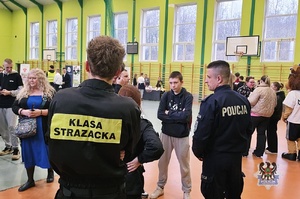 Na zdjęciu policjant w obecności uczestników spotkania promocyjnego.