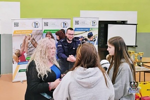 Na zdjęciu policjant w obecności uczestników spotkania promocyjnego.