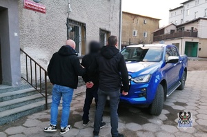 Na zdjęciu nieumundurowani policjanci i zatrzymany mężczyzna przy nieoznakowanym radiowozie.