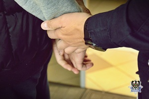 Na zdjęciu policjant zakłada kajdanki przykładowemu zatrzymanemu.