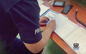 policjant wypełniający książkę  badania alkomatem