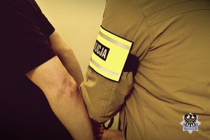 Nieumundurowany policjant zakłada kajdanki zatrzymanej osobie