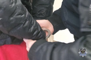 Na zdjęciu policjant zakłada kajdanki zatrzymanej osobie.