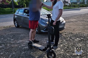 Na zdjęciu policjant, badany kierujący, hulajnoga oraz nieoznakowany radiowóz.