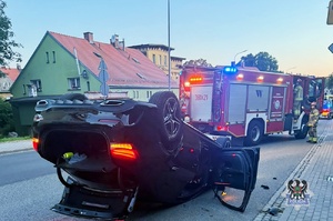 Na zdjęciu uszkodzony w wyniku dachowania samochód osobowy oraz służby ratownicze.