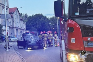 Na zdjęciu uszkodzony w wyniku dachowania samochód osobowy oraz służby ratownicze.