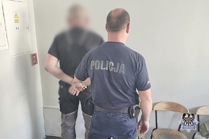 Na zdjęciu policjant pilnuje zatrzymanego mężczyzny.