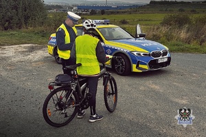 Na zdjęciu radiowóz oraz policjanci podczas kontroli drogowej.