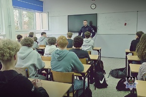Na zdjęciu policjant rozmawia z młodzieżą w szkole.