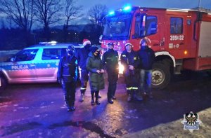 Pamiątkowe zdjęcie mundurowych przy wozie strażackim i radiowozie policyjnym.