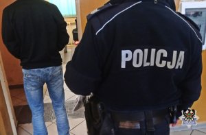 Na zdjęciu policjant pilnuje zatrzymanego mężczyzny.