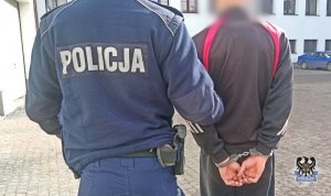 Na zdjęciu policjant prowadzi trzeciego z zatrzymanych mężczyzn.