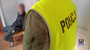 Na zdjęciu policjant pilnuje zatrzymanego mężczyzny.