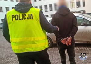 Na zdjęciu policjant prowadzi zatrzymanego mężczyznę.