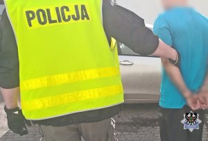 Na zdjęciu policjant prowadzi zatrzymanego mężczyznę do radiowozu.