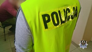 Na zdjęciu policjant pilnuje jednego z zatrzymanych mężczyzn.