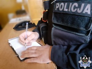 Policjant wpisuje dane do do notatnika służbowego