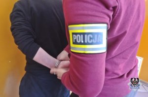 Na zdjęciu policjant zakłada kajdanki zatrzymanemu mężczyźnie.